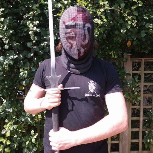 Member of the Academy of Steel wearing a black Academy t-shirt and a fencing mask with the Academy logo sprayed onto it.