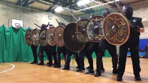 Academy of Steel members lined up in a shield wall with viking shields.